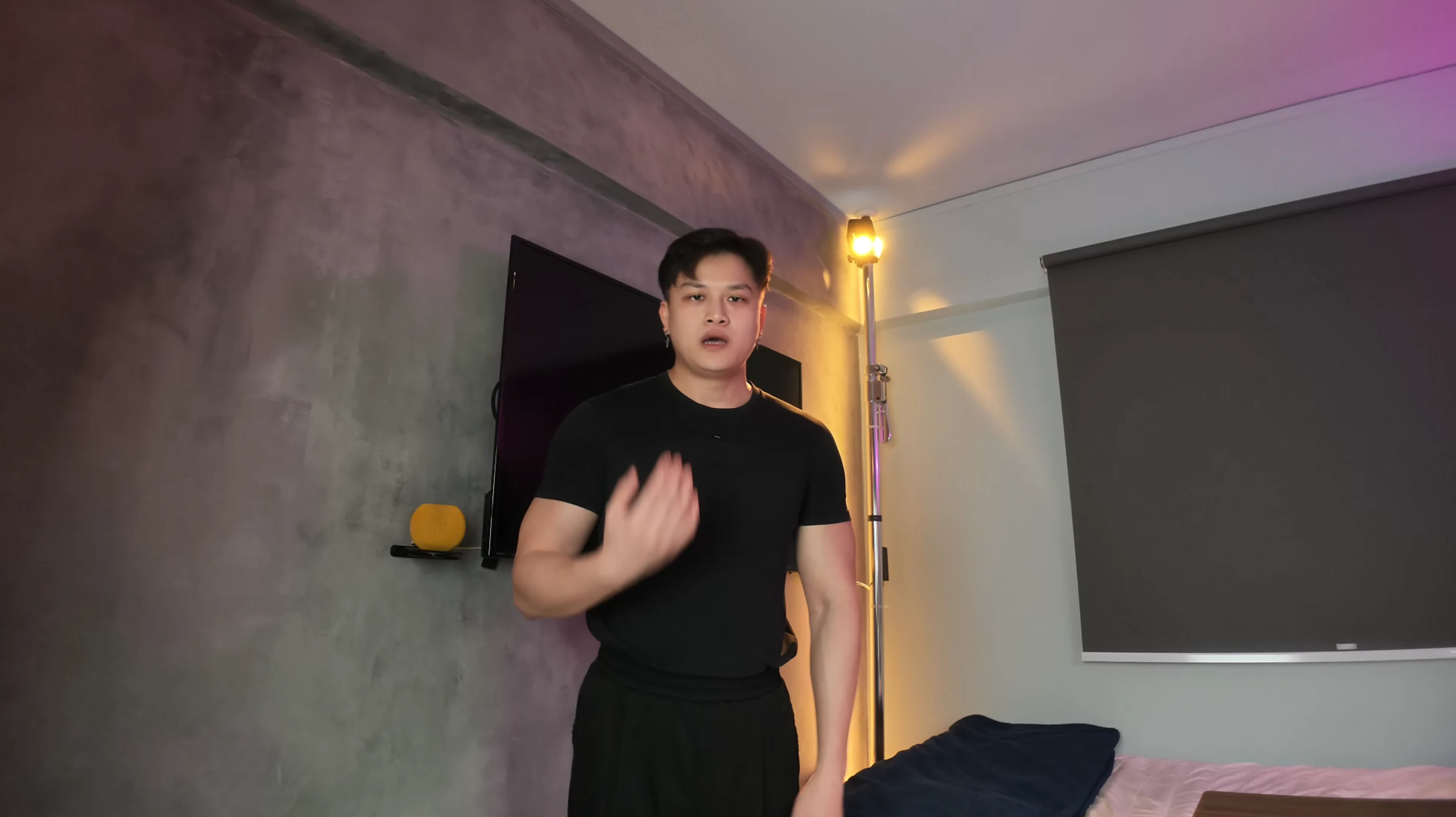 SIA standing in a room wearing black, with one hand raised near his chest.